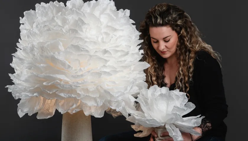 Laura Druart présentant sa lampe fleur La Majestueuse, une création artisanale aux pétales blancs.